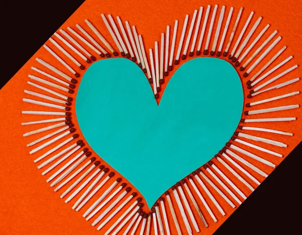 Yanmamış kibritle kaplanmış bir kalp şekli. Seçici odaklanma, metin için yer. Mavi kalp, turuncu arka planda siyah üçgenlerle eşleştirilmiş. Seçici odak, metin için yer,