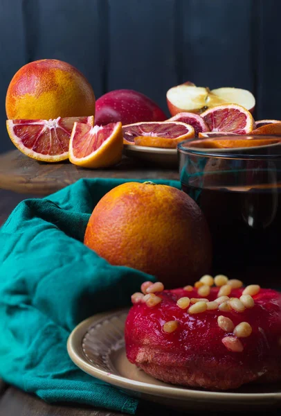 Kanlı Sicilya portakalları ahşap masada çay ve çam fıstığıyla kaplı kırmızı kremayla kaplı donut. Seçici odaklanma. Boşluğu kopyala, kenar görünüm