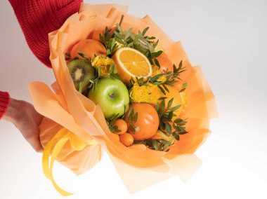 Tatil için mandalinalı ve yeşil elmalı yenilebilir buket. Ellerinde beyaz bir arka planda.