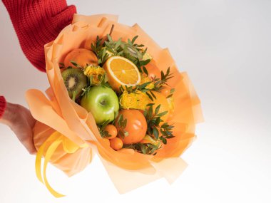 Tatil için mandalinalı ve yeşil elmalı yenilebilir buket. Ellerinde beyaz bir arka planda.