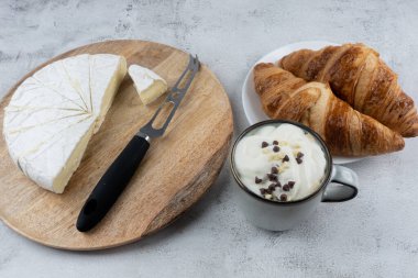 Bir fincan kahve, tereyağlı çörek, peynir bıçağı ve tahta tabakta dilimlenmiş beyaz peynir. Ev kahvaltısı
