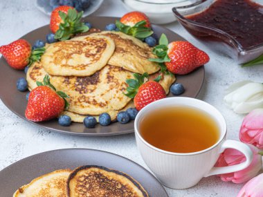 Yabanmersinli, çilekli, reçelli ve ekşi kremalı ev yapımı krep. Beyaz arka planda çay, yukarıdan manzara. Kahvaltı, atıştırmalık ve beslenme konsepti. Maslenitsa.