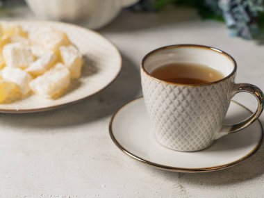 Masada bir çaydanlık ve beyaz bir kupa, çiçekler ve tabakta pudra şekerli geleneksel Türk ve Yunan reçeli şekerlemeleri. Arapça şekerlemeler
