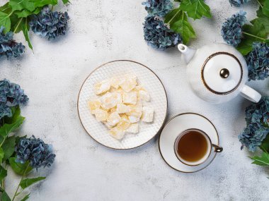 Masada bir çaydanlık ve beyaz bir kupa, çiçekler ve tabakta pudra şekerli geleneksel Türk ve Yunan reçeli şekerlemeleri. Arapça şekerlemeler