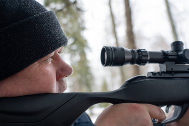 Bahar ormanında tüfekli bir adam, avcı tüfeğini tutar ve avını bekler, avcı ateş eder.