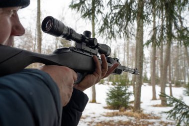 Bahar ormanında tüfekli bir adam, avcı tüfeğini tutar ve avını bekler, avcı ateş eder.