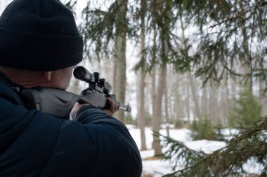 Bahar ormanında tüfekli bir adam, avcı tüfeğini tutar ve avını bekler, avcı ateş eder.
