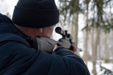 Bahar ormanında tüfekli bir adam, avcı tüfeğini tutar ve avını bekler, avcı ateş eder.