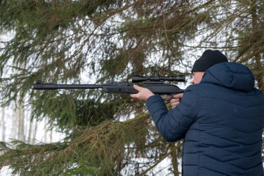 Bahar ormanında tüfekli bir adam, avcı tüfeğini tutar ve avını bekler, avcı ateş eder.