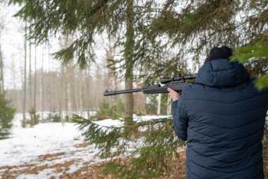 Bahar ormanında tüfekli bir adam, avcı tüfeğini tutar ve avını bekler, avcı ateş eder.