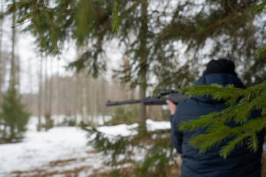 Bahar ormanında tüfekli bir adam, avcı tüfeğini tutar ve avını bekler, avcı ateş eder.