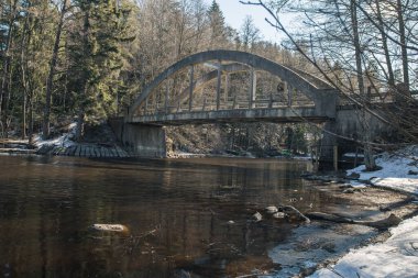 Bir orman nehrinin Nisan ayında nehir boyunca uzanan eski bir köprü. Kıyıda kar var. Finlandiya.