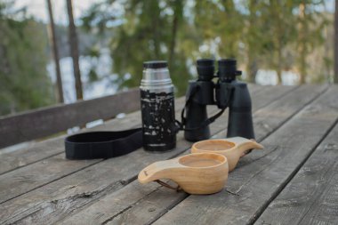 Bahar ormanı. Masanın üzerinde dürbün, termos ve kahve kupaları var..