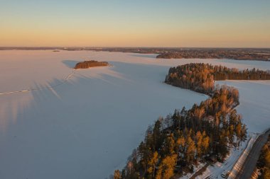 Ormanın üzerindeki manzara ve buzla kaplı göl. Kışın erken doğumu. Drone fotoğrafı. İskandinavya. Finlandiya.