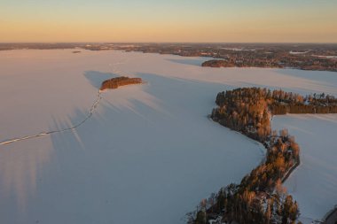 Ormanın üzerindeki manzara ve buzla kaplı göl. Kışın erken doğumu. Drone fotoğrafı. İskandinavya. Finlandiya.