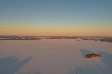Ormanın üzerindeki manzara ve buzla kaplı göl. Kışın erken doğumu. Drone fotoğrafı. İskandinavya. Finlandiya.
