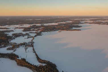 Ormanın üzerindeki manzara ve buzla kaplı göl. Kışın erken doğumu. Drone fotoğrafı. İskandinavya. Finlandiya.