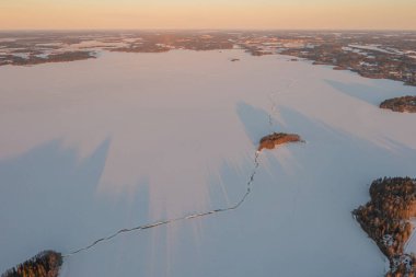 Ormanın üzerindeki manzara ve buzla kaplı göl. Kışın erken doğumu. Drone fotoğrafı. İskandinavya. Finlandiya.