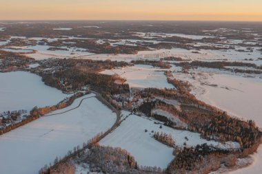 Ormanın üzerindeki manzara ve buzla kaplı göl. Kışın erken doğumu. Drone fotoğrafı. İskandinavya. Finlandiya.