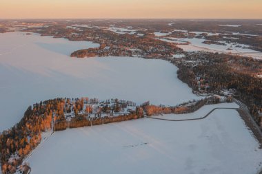 Ormanın üzerindeki manzara ve buzla kaplı göl. Kışın erken doğumu. Drone fotoğrafı. İskandinavya. Finlandiya.