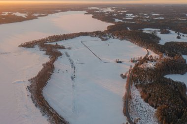 Ormanın üzerindeki manzara ve buzla kaplı göl. Kışın erken doğumu. Drone fotoğrafı. İskandinavya. Finlandiya.