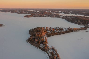 Ormanın üzerindeki manzara ve buzla kaplı göl. Kışın erken doğumu. Drone fotoğrafı. İskandinavya. Finlandiya.