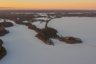 Ormanın üzerindeki manzara ve buzla kaplı göl. Kışın erken doğumu. Drone fotoğrafı. İskandinavya. Finlandiya.