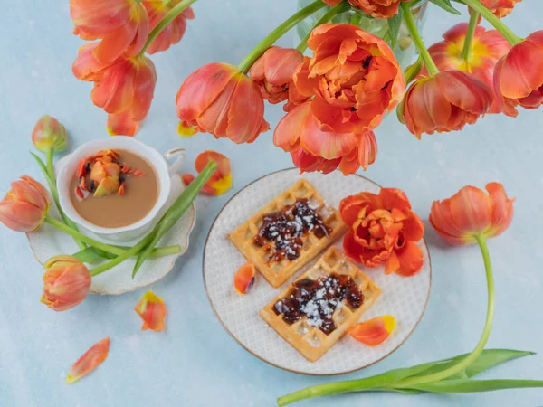 Scarlet, red tulips in a vase and a white cup with coffee and French waffles. The concept of congratulations and old holidays. There is a place for text.