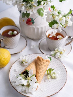 Beyaz çay seti, fincanlarda çay, sarı limonlar ve çiçek açan bir elma dalı. Yukardan bakıldığında, çay tabağında waffle konileri var..