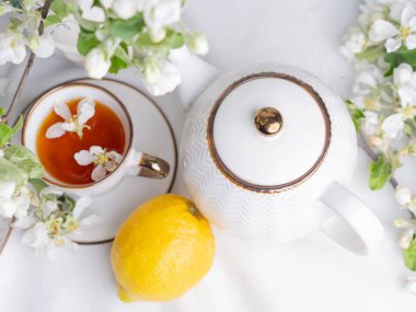 Beyaz çay seti, fincanlarda çay, sarı limonlar ve çiçek açan elma dalıyla. Kapalı tabakta waffle konileri var..