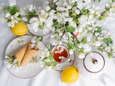 Beyaz çay seti, fincanlarda çay, sarı limonlar ve çiçek açan bir elma dalı. Yukardan bakıldığında, çay tabağında waffle konileri var..