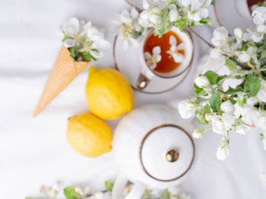 Beyaz çay seti, fincanlarda çay, sarı limonlar ve çiçek açan bir elma dalı. Yukardan bakıldığında, çay tabağında waffle konileri var..