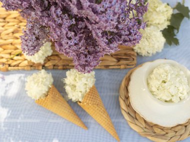 Bir buket leylak, sepette beyaz viburnum ve çay seti. Bahçedeki masada, arka plan beyaz.