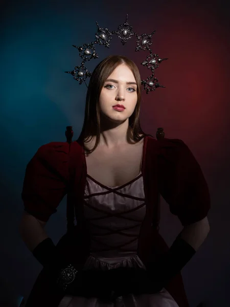 Mythical fantasy queen. Silvery gothic crown on the head. Burgundy vintage artistic dress, black gloves and vintage bracelet. Elven princess. Medieval style. Medium shot portrait in a dark key.