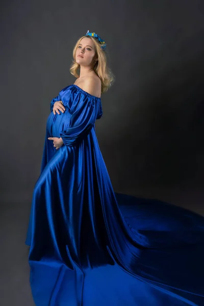 一个怀孕的女孩 穿着蓝色长裙 头带蝴蝶 在黑暗背景上的全长照片快乐怀孕的概念 — 图库照片