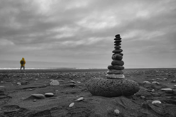 Небольшая Каменная Башня Черном Пляже Исландии Мужчиной Желтом Плаще Заднем — стоковое фото