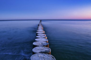 Güneş doğmadan birkaç dakika önce Baltık Denizi 'nde donmuş ahşap bir dalgakıran.