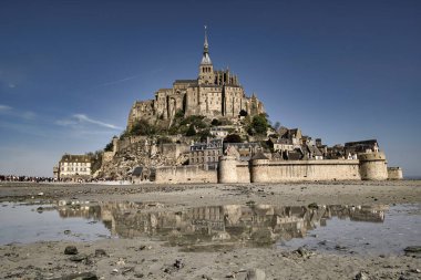 Güneşli bir günde mavi gökyüzü ve yansımalarıyla ünlü tarihi Le Mont Saint-Michel gelgit adasının panoramik manzarası