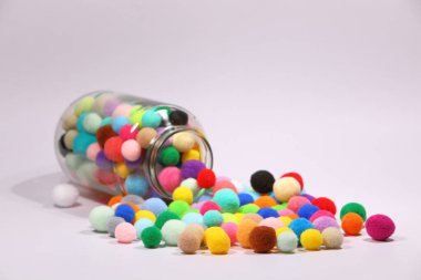 Beyaz arka planda cam şişelerden akan renkli ponponlar.