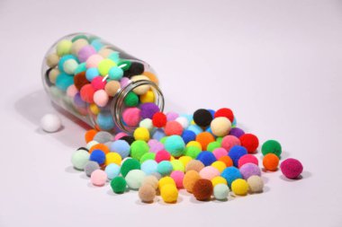 Beyaz arka planda cam şişelerden akan renkli ponponlar.