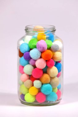 Beyaz arka planda cam şişede renkli ponpon.