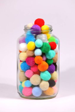 Beyaz arka planda cam şişede renkli ponpon.