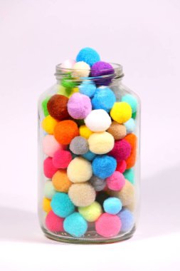 Beyaz arka planda cam şişede renkli ponpon.