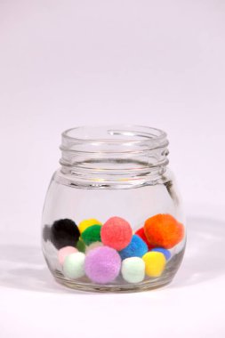 Beyaz arka planda cam şişede renkli ponpon.