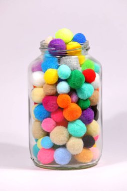 Beyaz arka planda cam şişede renkli ponpon.