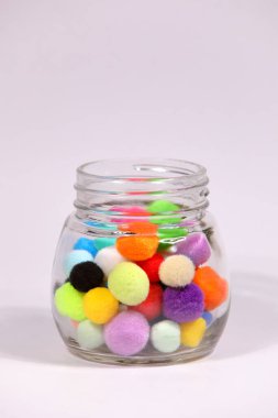 Beyaz arka planda cam şişede renkli ponpon.