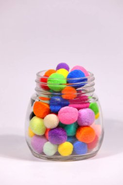 Beyaz arka planda cam şişede renkli ponpon.