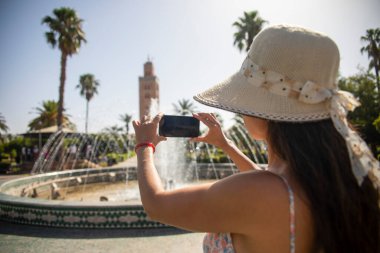 Lalla Hasna parkındaki cep telefonlu kadın Fas 'ın Marakeş kentindeki Koutoubia Camii' nin muhteşem manzarasını ve panoramik manzarasını çekiyordu..