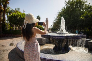 Lalla Hasna parkından cep telefonlu bir turist Fas 'taki Marakeş şehrindeki Koutoubia Camii' nin muhteşem manzarasını ve panoramik manzarasını çekerken görülüyor..