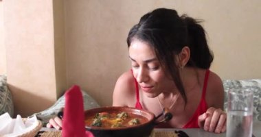 Güzel bir turist kadın Fas dekorasyonuyla süslenmiş bir restoranda lezzetli bir tabak Marakeş Arap köftesi yerken yemek ve kokluyor..